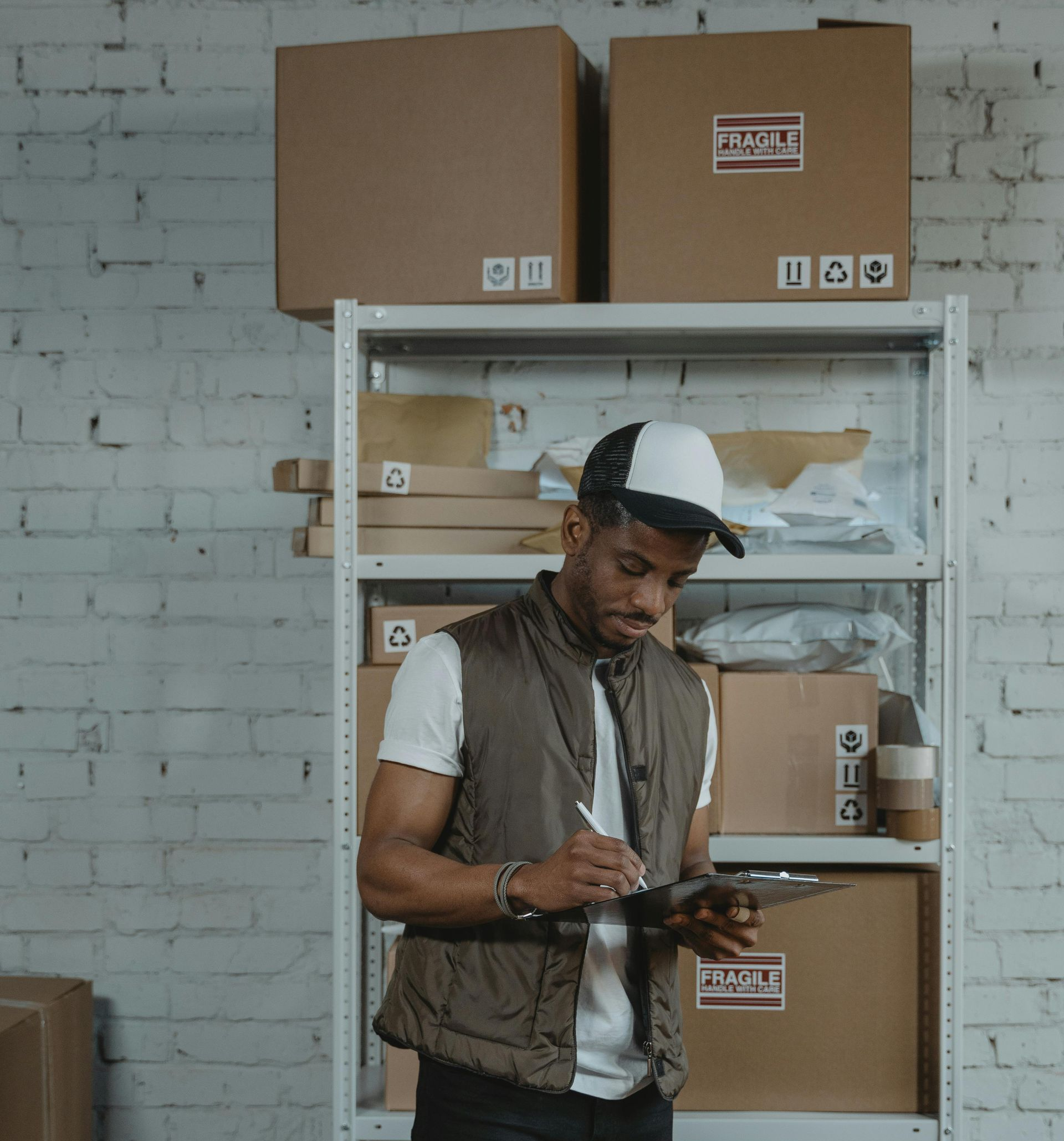 Person writing on a tablet in a storage room with shelves and cardboard boxes.