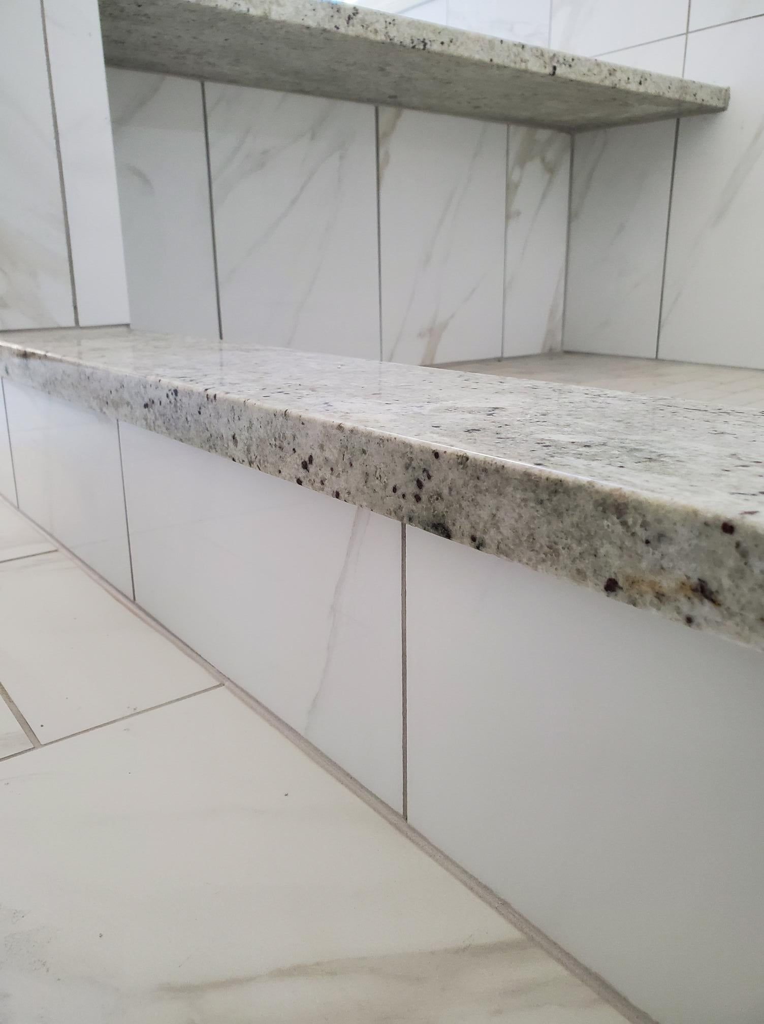 A bathroom with white tiles and a granite counter top.