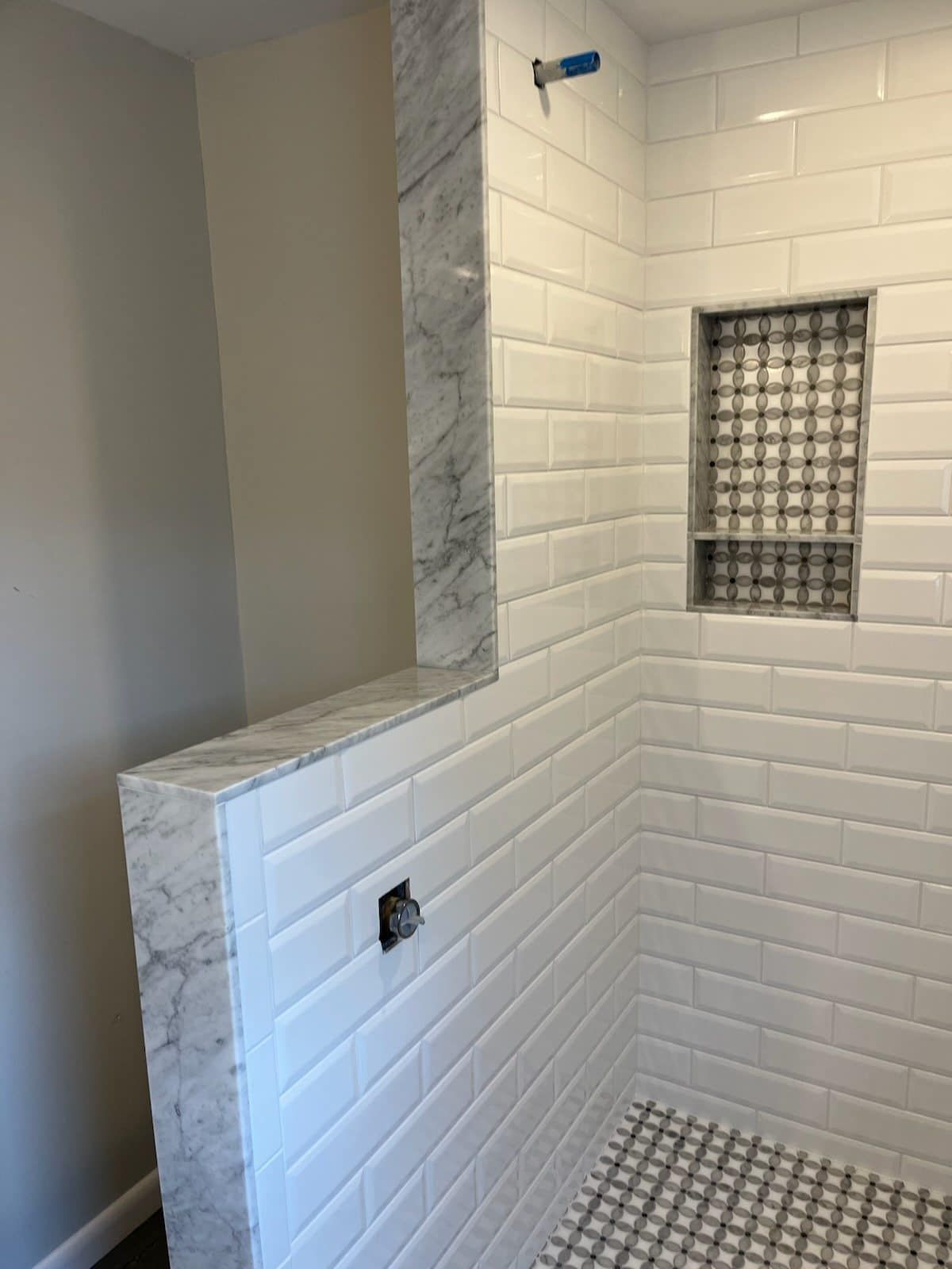 A shower with white tiles and a marble counter top.