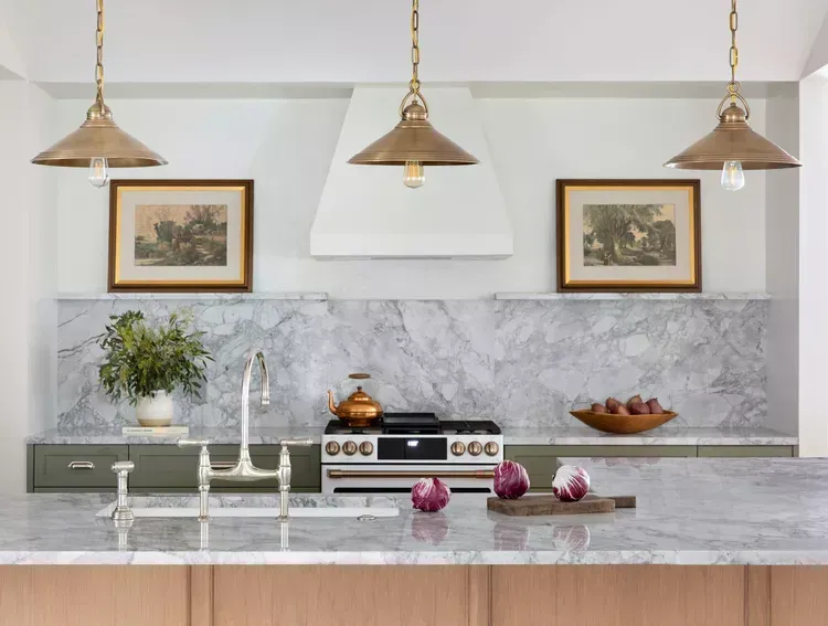 A kitchen with a stove , sink , and three lamps hanging from the ceiling.