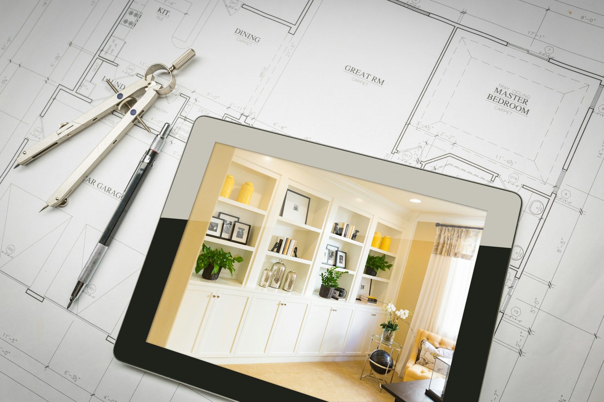 A tablet displaying an interior design photo placed over architectural blueprints with drafting tool