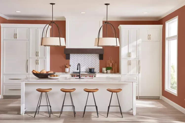 A kitchen with white cabinets and red walls has a large island in the middle. A kitchen with white cabinets and red walls has a large island in the middle.