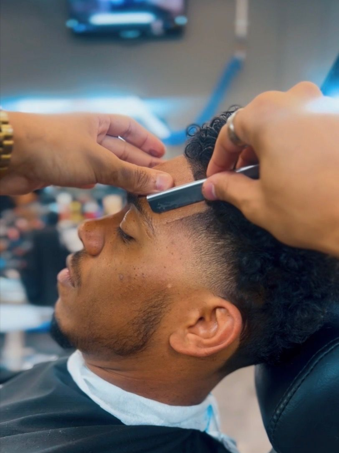 Barber shaping a client's hairline with a straight razor in a barbershop.
