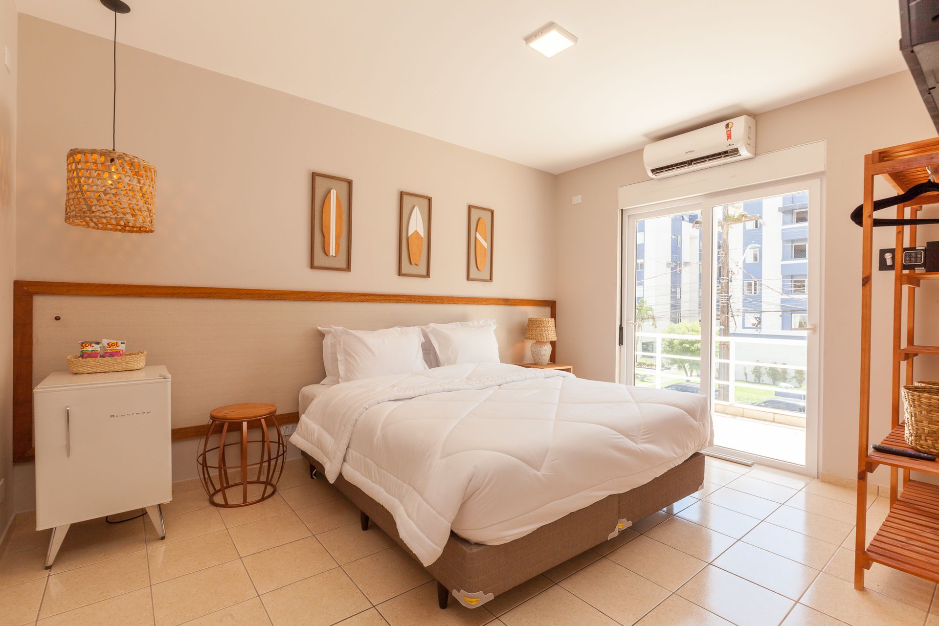 Quarto com cama branca, paredes bege e porta de vidro deslizante.