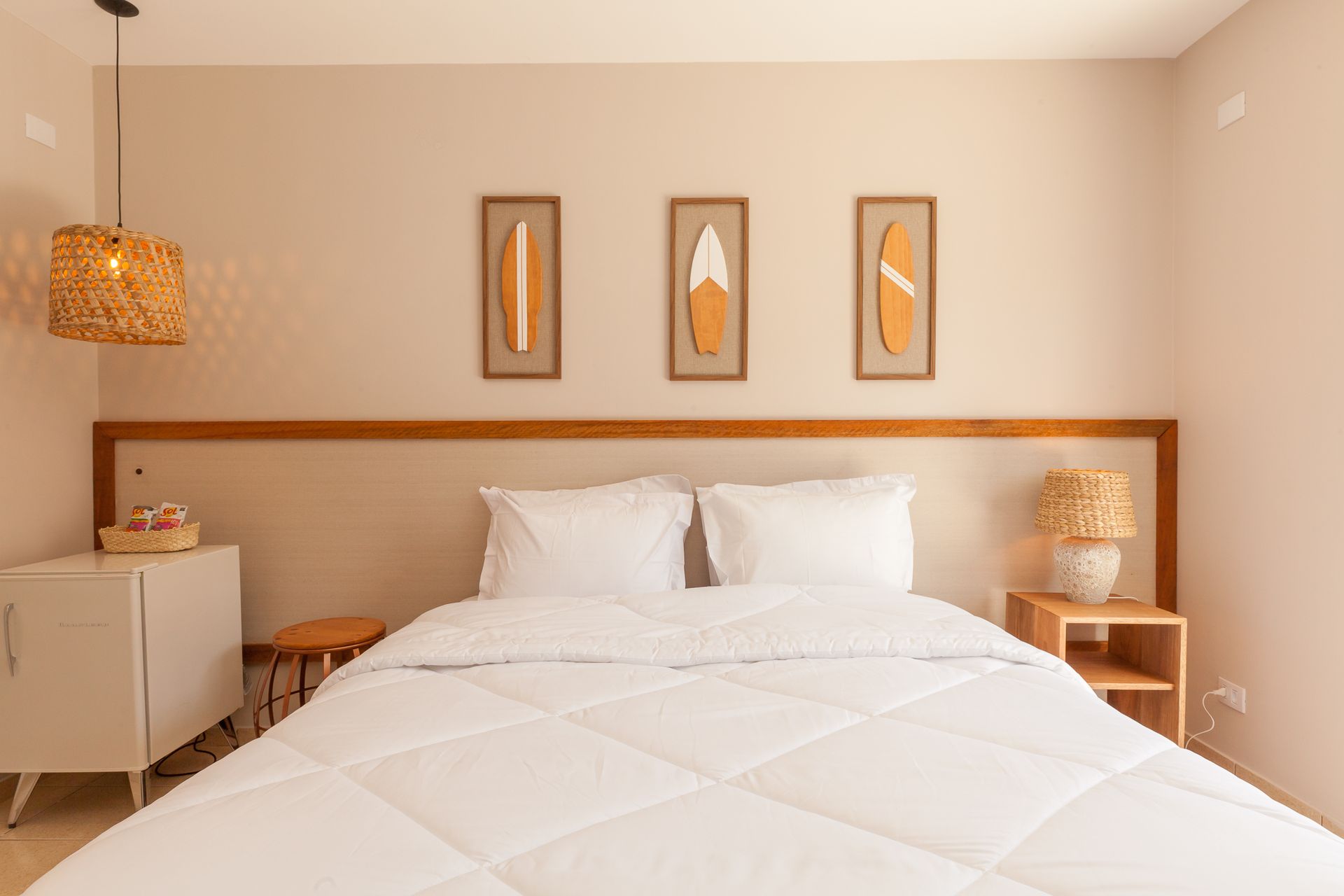 Quarto com cama, arte em forma de prancha de surfe, luminárias de vime e uma pequena mesa de cabeceira.