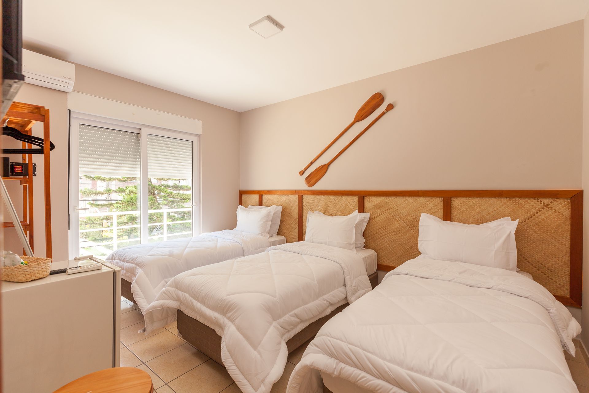 Quarto com três camas de solteiro, roupa de cama branca, cabeceiras de madeira natural e remos na parede.