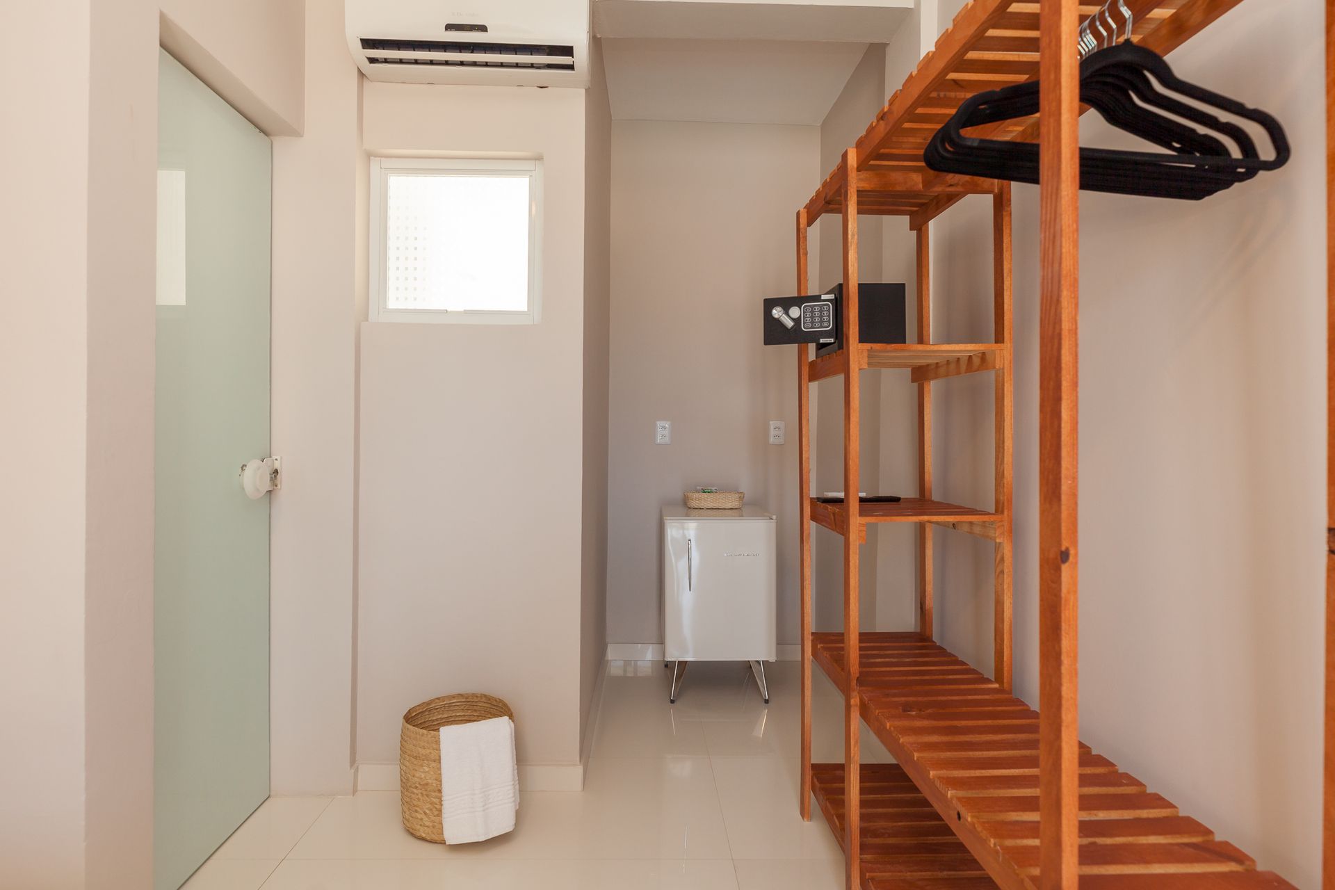 Corredor com uma prateleira de madeira, cofre, armário branco e uma porta à esquerda.
