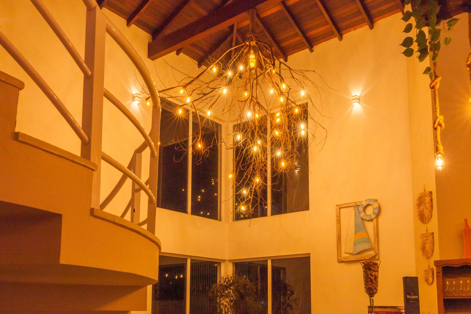 Interior com escada em espiral, janelas amplas e luminária decorativa com várias lâmpadas pendentes.