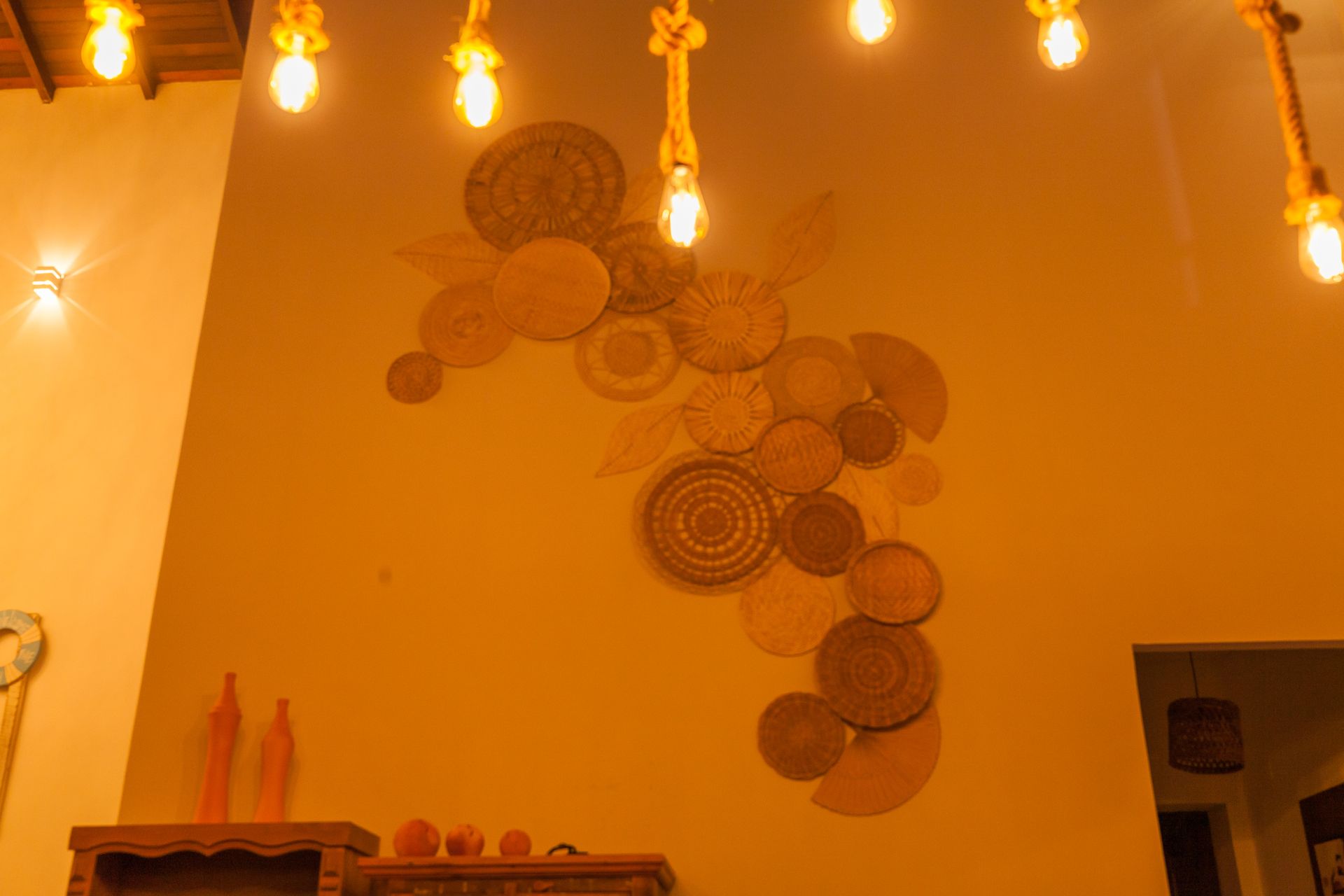 Decoração de parede composta por peças circulares trançadas com luzes pendentes.