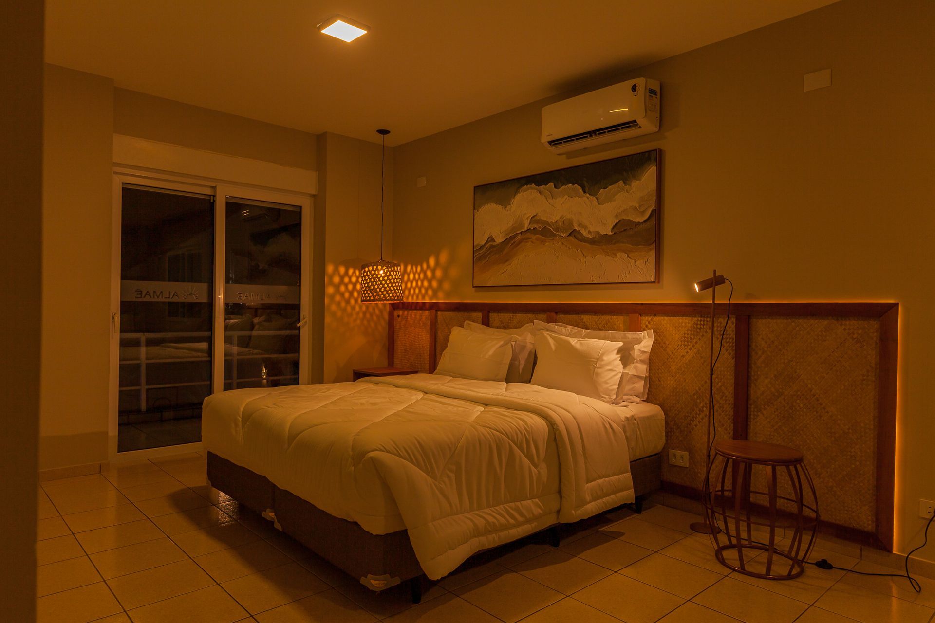 Quarto com cama, obras de arte e varanda visível através de uma porta de correr.