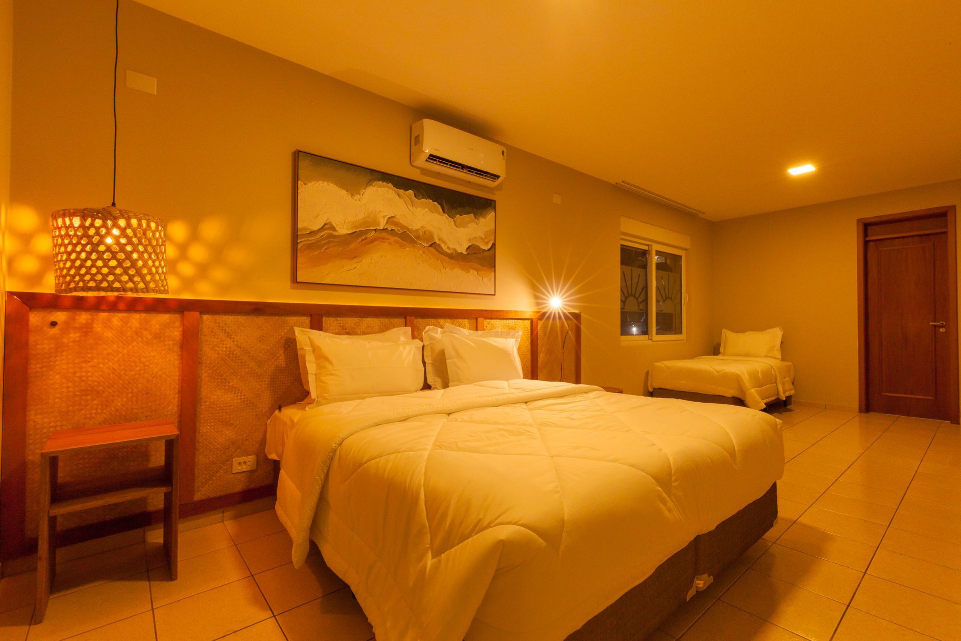 Quarto com cama de casal, poltrona, janela e iluminação aconchegante.