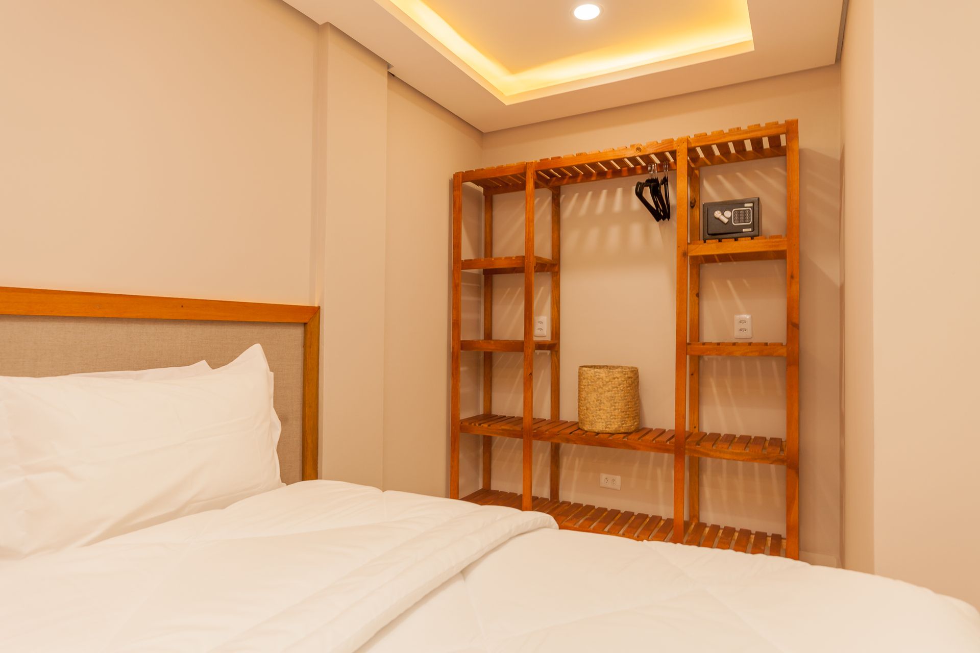 Quarto com cama, guarda-roupa aberto de madeira e iluminação no teto.
