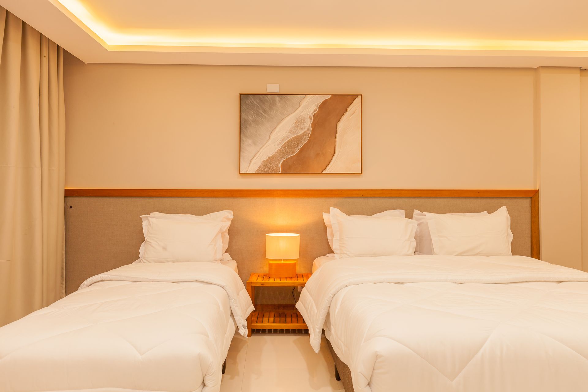 Quarto com duas camas e uma mesa de cabeceira, decoração em tons claros e obras de arte na parede.