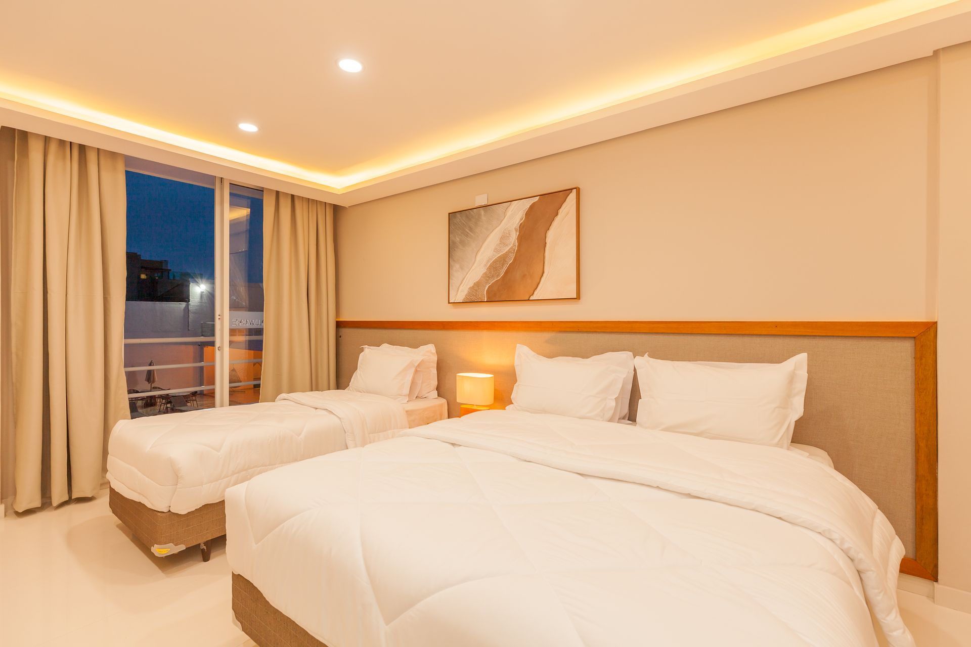 Quarto com duas camas, tons neutros, varanda com vista e obras de arte.