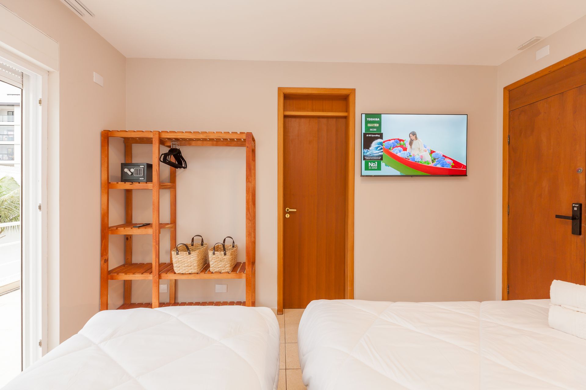 Quarto com duas camas, armário de madeira, TV e porta fechada.