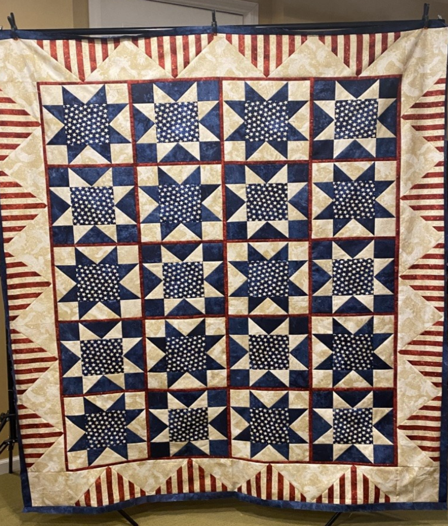 A red , white and blue quilt is hanging on a rack.