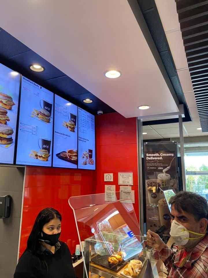 A man and a woman wearing masks are standing in a fast food restaurant.
