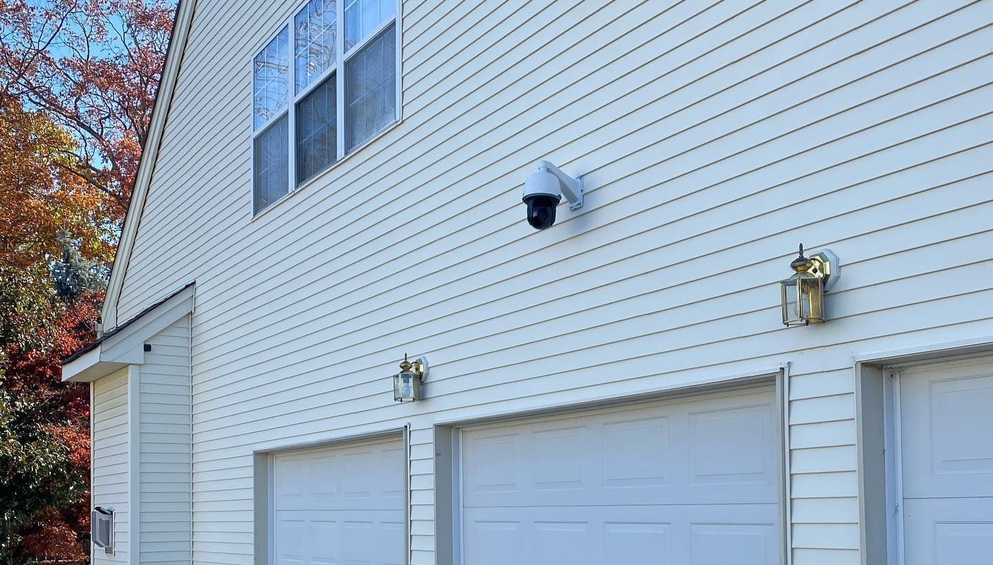 A white house with three garage doors and a security camera on the side.