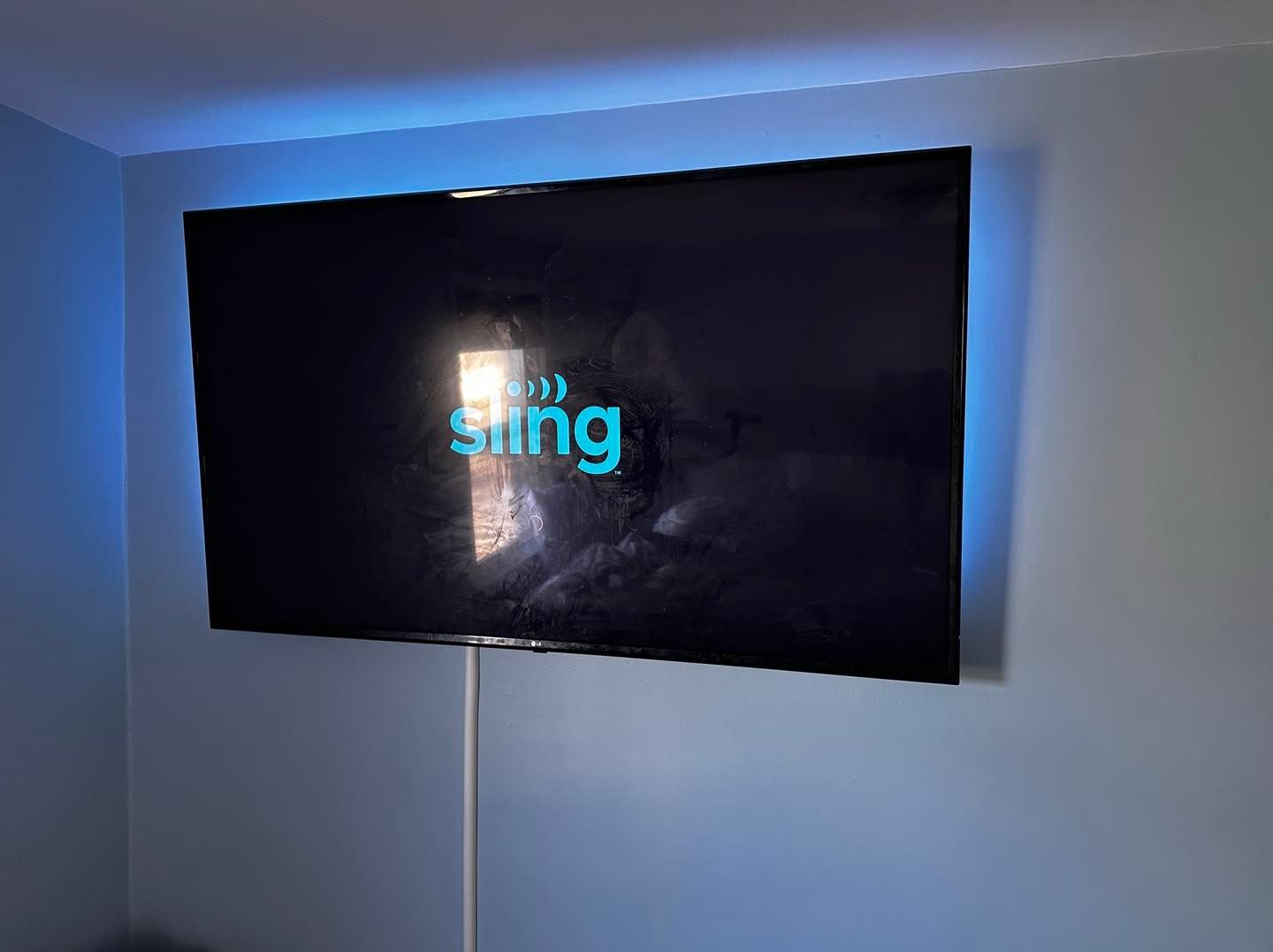 A flat screen tv is mounted on a wall with a sling logo on the screen.