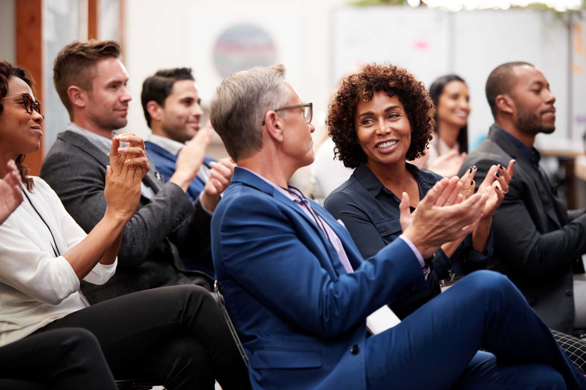 Audience applauding at a business event, with people seated in a bright conference room.