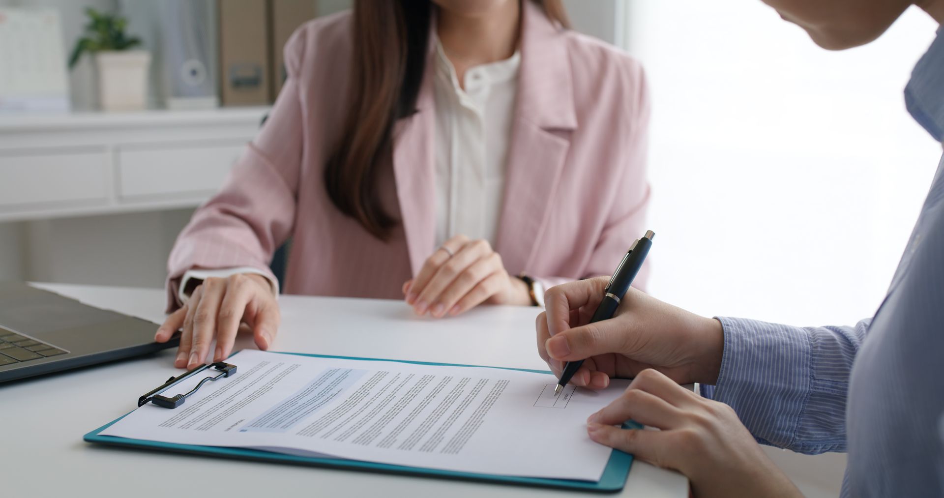 Two people signing a document at a desk during a meeting