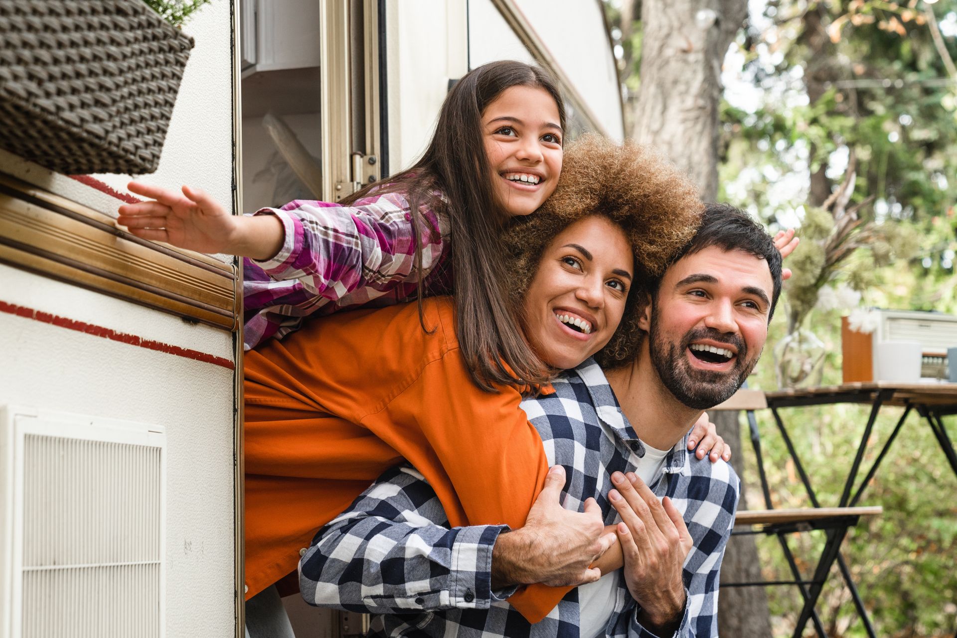 Three smiling friends posing outdoors on a porch, with one leaning over the others’ shoulders.
