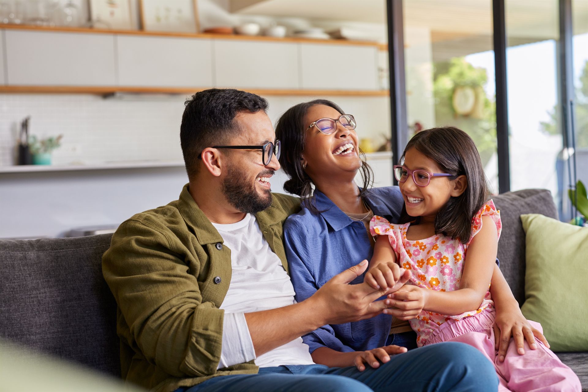 Three people smiling on a couch in a bright living room, sharing a happy moment.