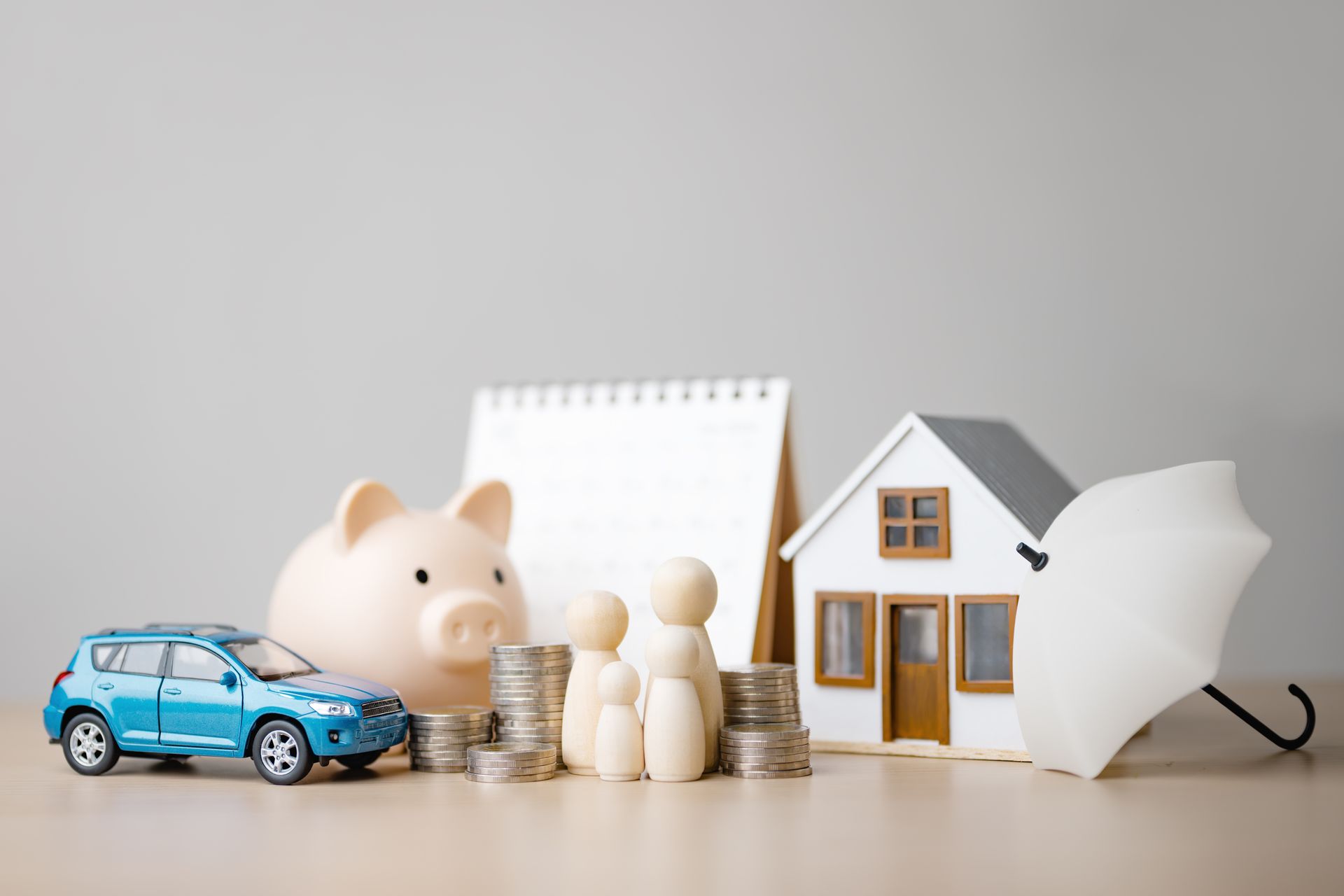 Blue toy car, piggy bank, coins, wooden figures, and a small house model on a table