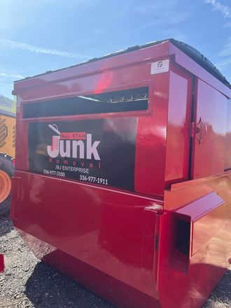 Red industrial dumpster trailer with a black Junk logo panel outdoors on gravel under a blue sky