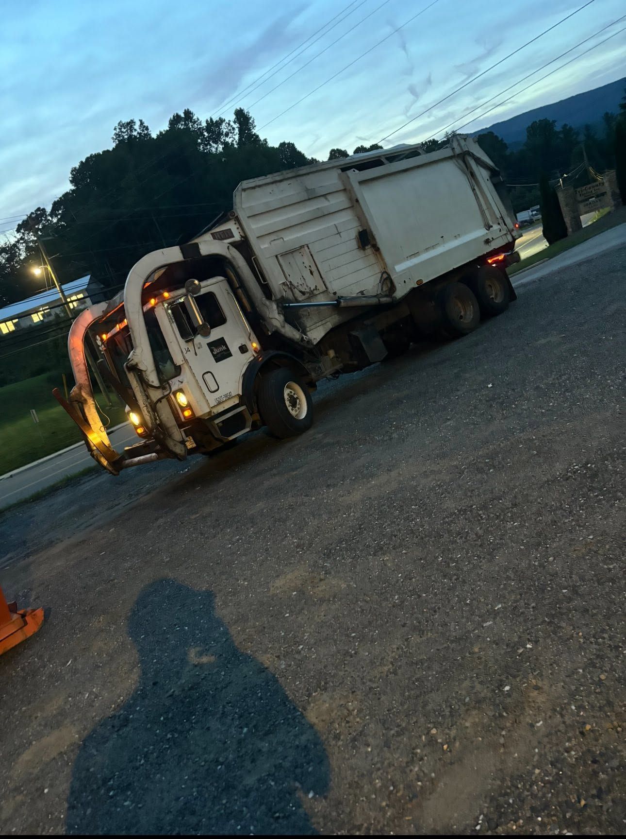 Tow truck towing a white dump truck on a gravel lot at dusk.