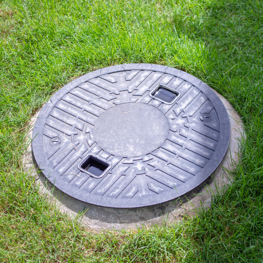 Round metal manhole cover set in green grass, with two rectangular openings.