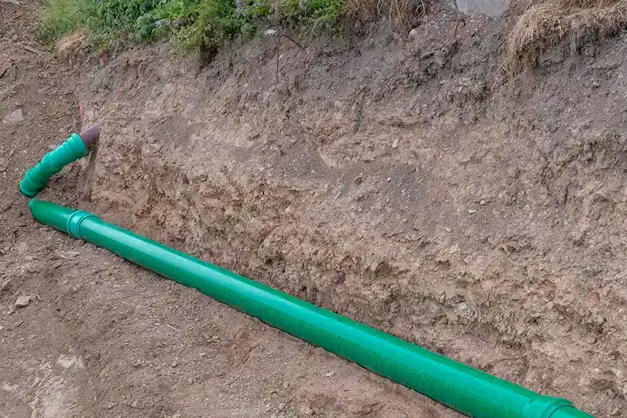 Green pipe laid in a dirt trench, with a bent section at the left edge.