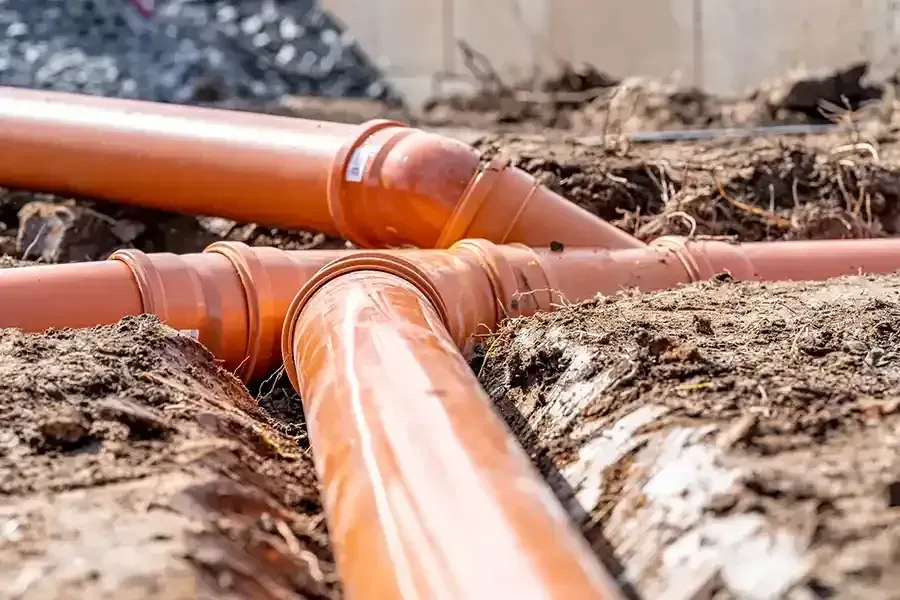 Orange PVC pipes connected in a trench during outdoor plumbing installation