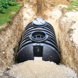 Black underground septic tank installed in a dirt trench with exposed access lids.