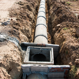 Trench with a large buried pipe leading into a square concrete drainage box