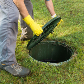 Worker lifting a green manhole cover from a round opening in a grassy lawn
