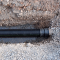 Black corrugated pipe laid in a trench surrounded by dirt and gravel
