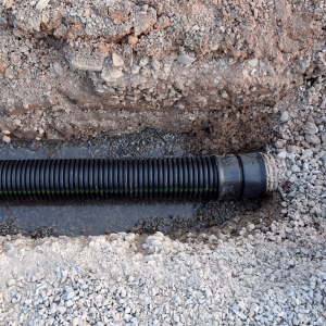 Black corrugated pipe laid in a trench surrounded by dirt and gravel