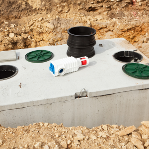 Concrete utility box with black and green pipe fittings on dirt ground at a construction site