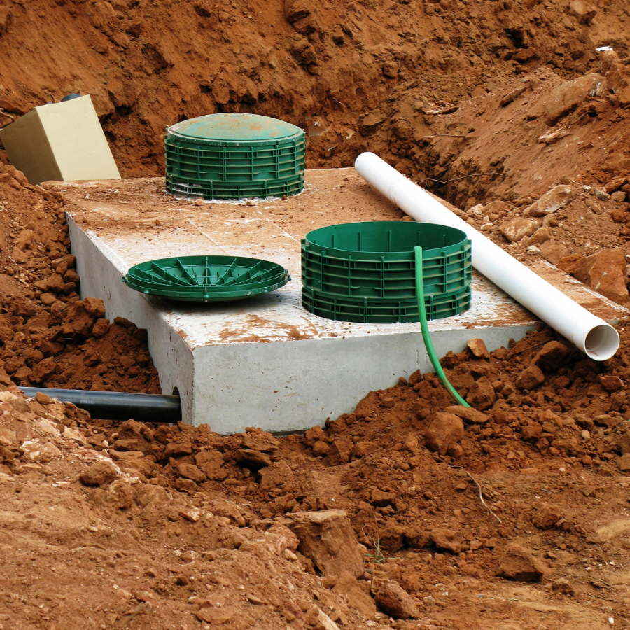 Worker in blue and yellow gear lowering a hose into an open manhole on grass.