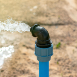 Blue pipe with black elbow joint expelling water outdoors onto sand.
