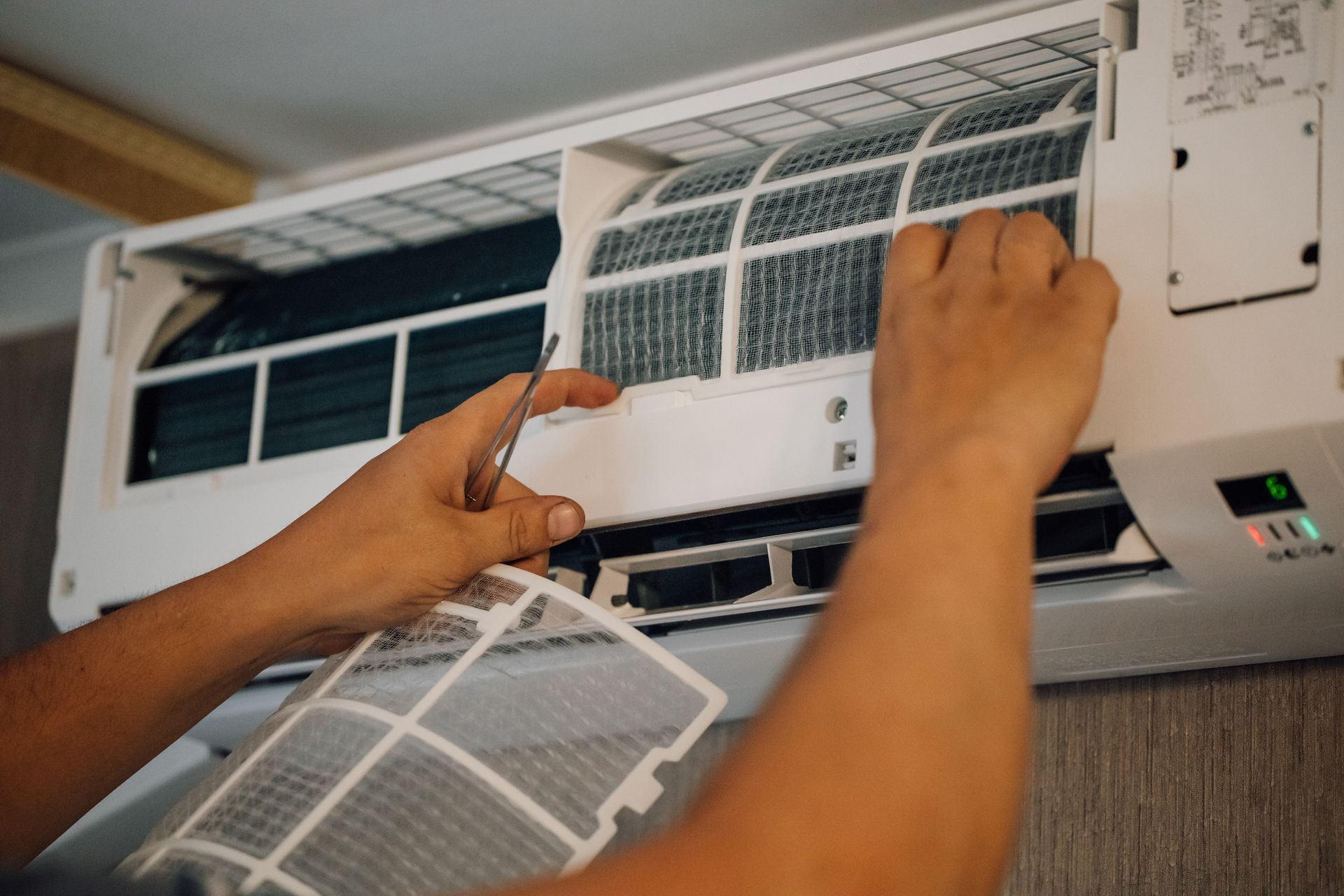 A person is fixing an air conditioner with a screwdriver.