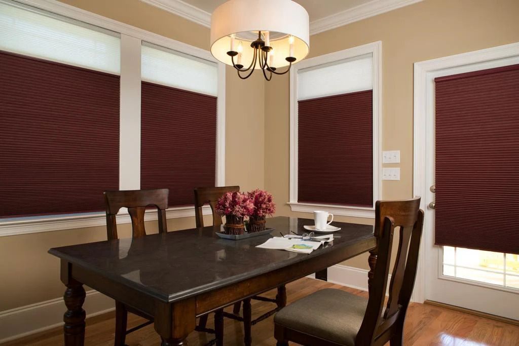 Dining room with dark wood table, chairs, and burgundy window shades under a chandelier.