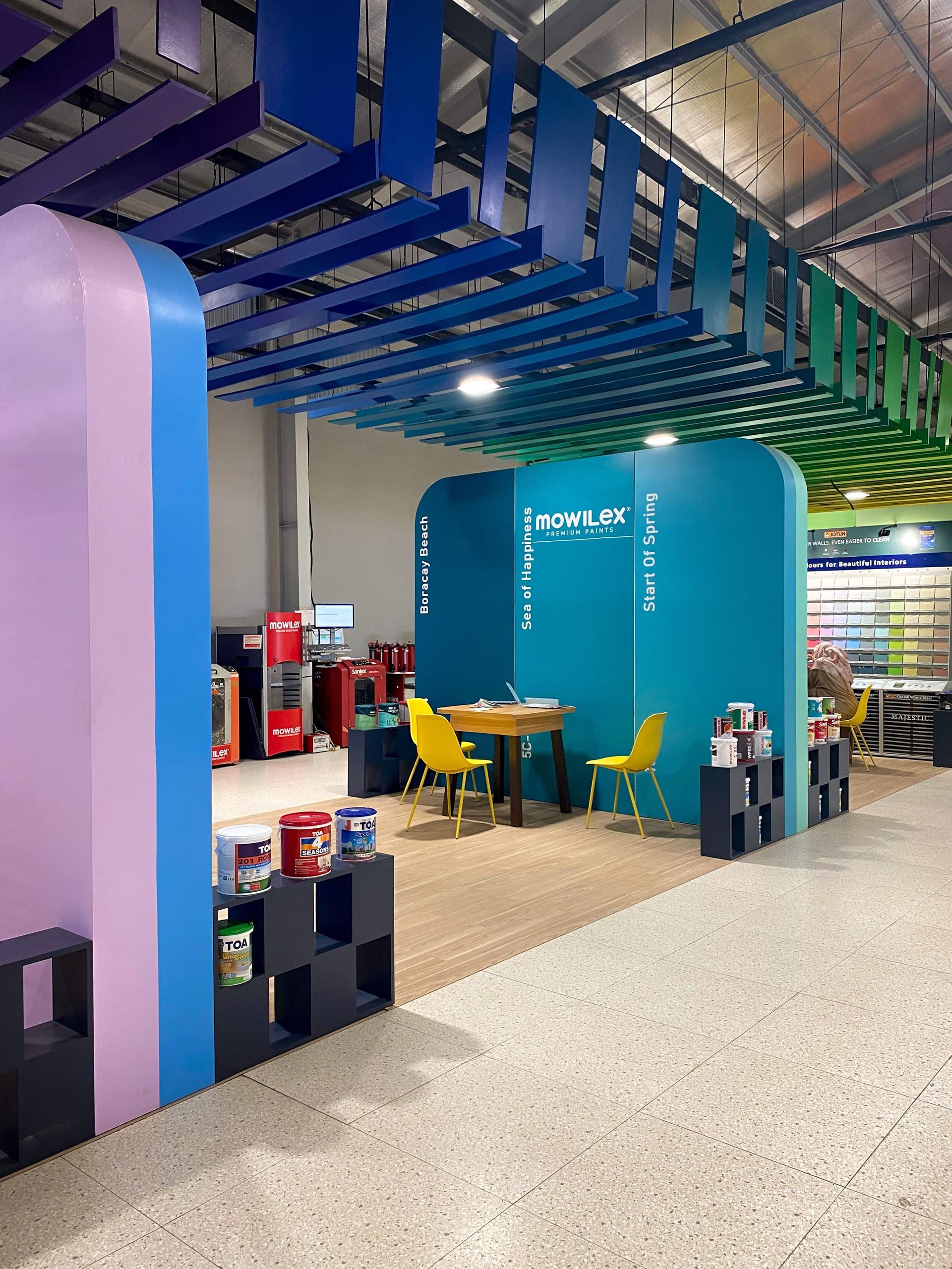 Modern retail display with blue ceiling slats, teal wall, chairs, and product stands in a store interior