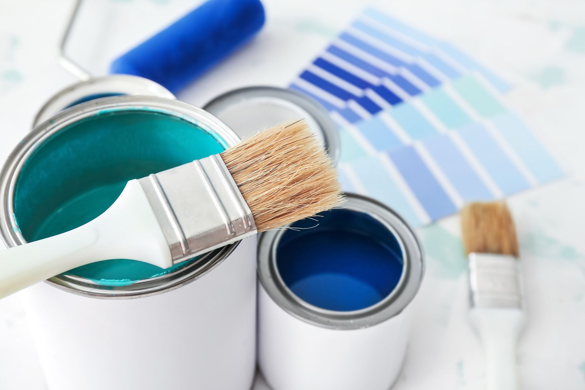 Paintbrushes in open paint cans with blue and teal paint, on a white surface