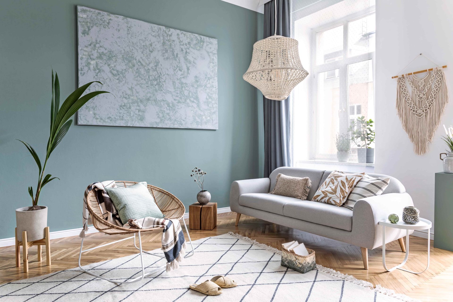 Bright modern living room with gray sofa, woven chair, teal wall, large window, and geometric rug
