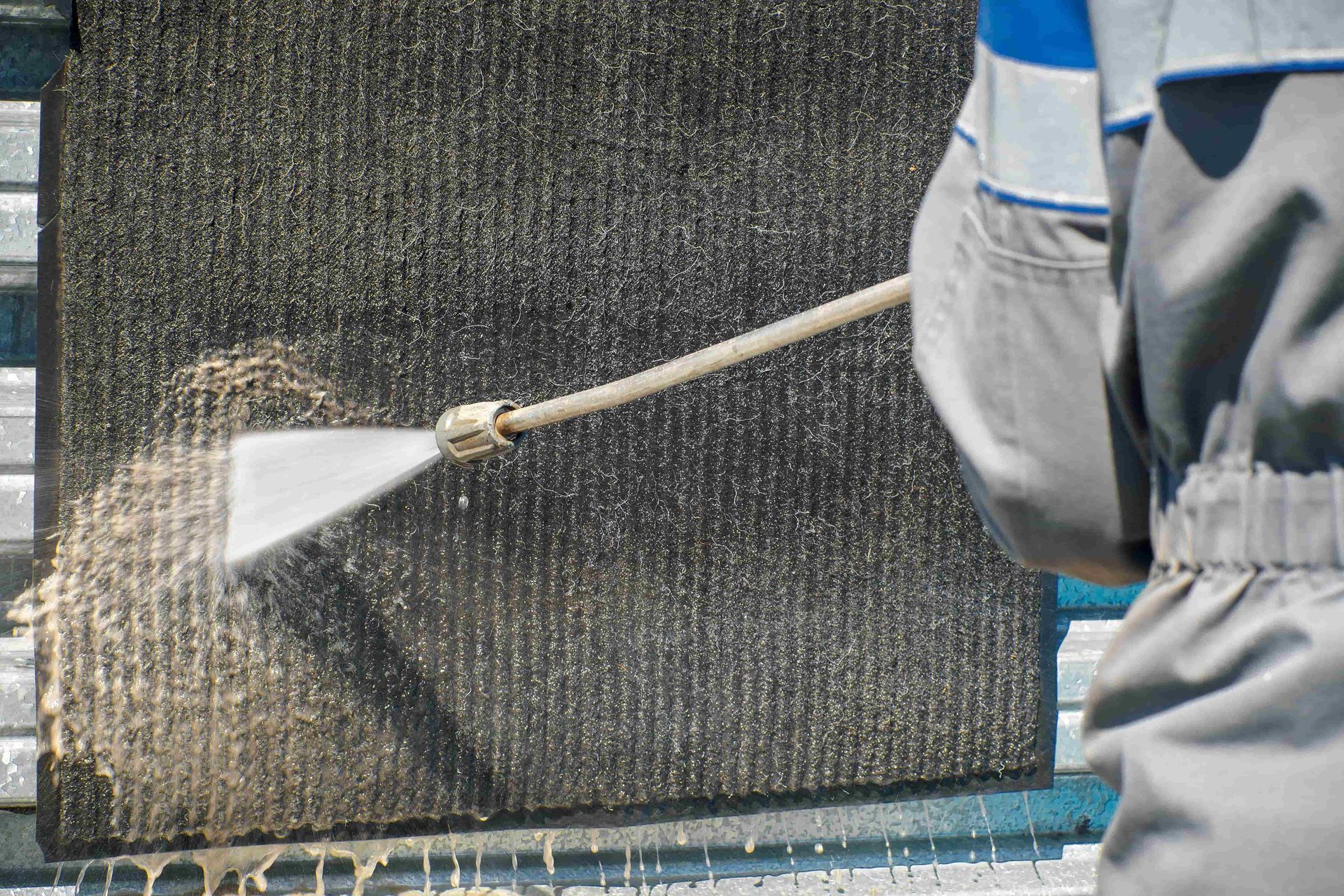 Worker pressure-washing a dark exterior wall with a spray nozzle