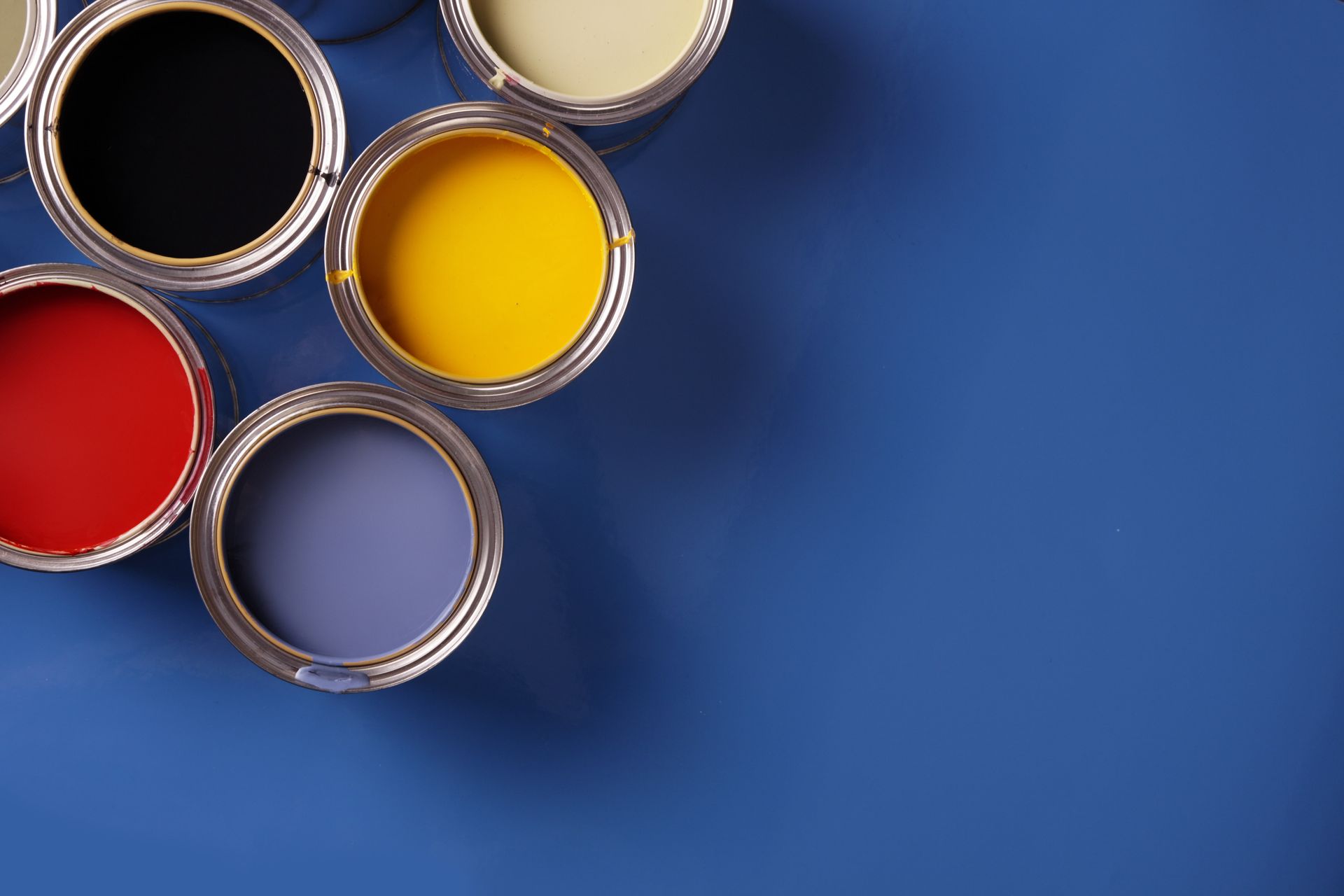 Five open paint cans with black, red, yellow, and blue paint on a blue background