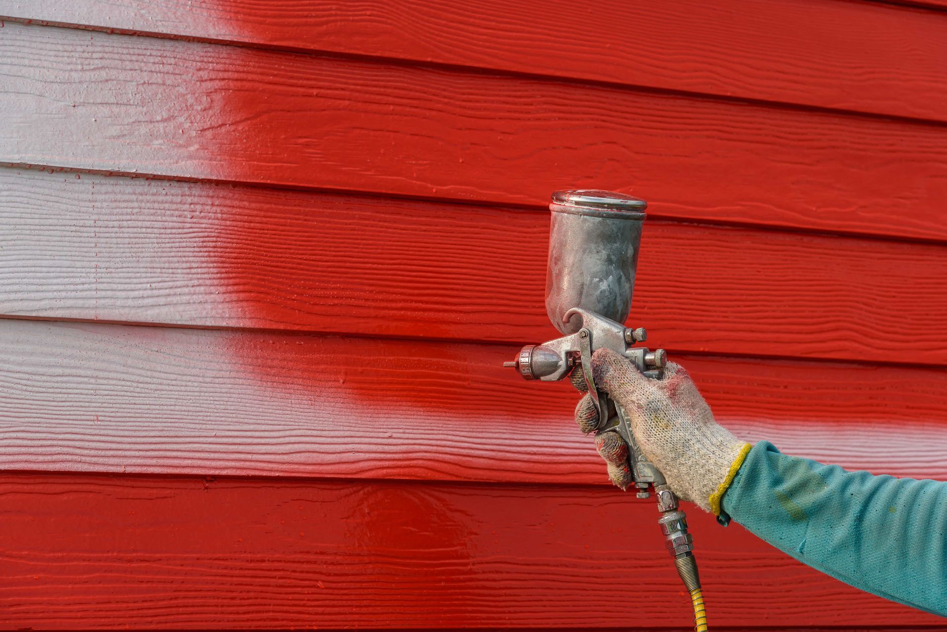 Person spray-painting a red wooden wall with a paint sprayer