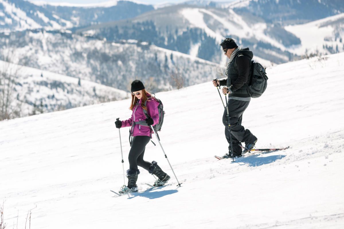 Two people snowshoeing uphill on a snowy slope with a mountain backdrop.